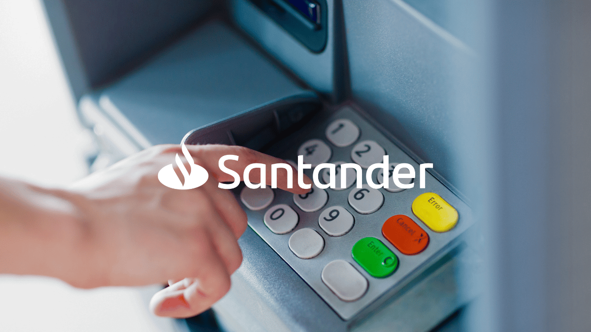 Imagem de uma pessoa (apenas mostrando a mãos) digitando no caixa eletrônico. O logo do Santander está logo a frente.