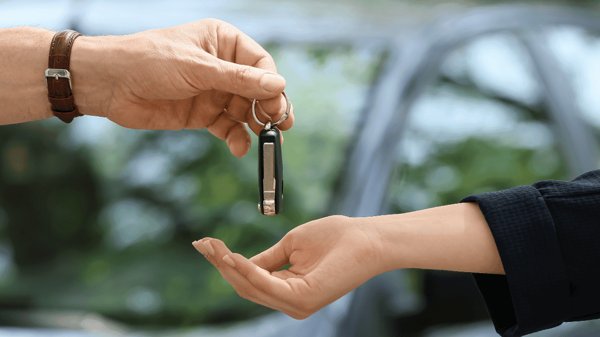 Imagem de um homem dando uma chave de carro para uma mulher (ambos só mostram a mão e o braço).