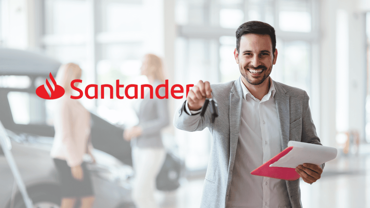 Imagem de um homem branco com cabelo e barba moreno e usando um terno cinza. Ele está em uma concessionária segurando a chave de um carro, uma prancheta e sorrindo. Ao lado dele, está o logo do Santander.